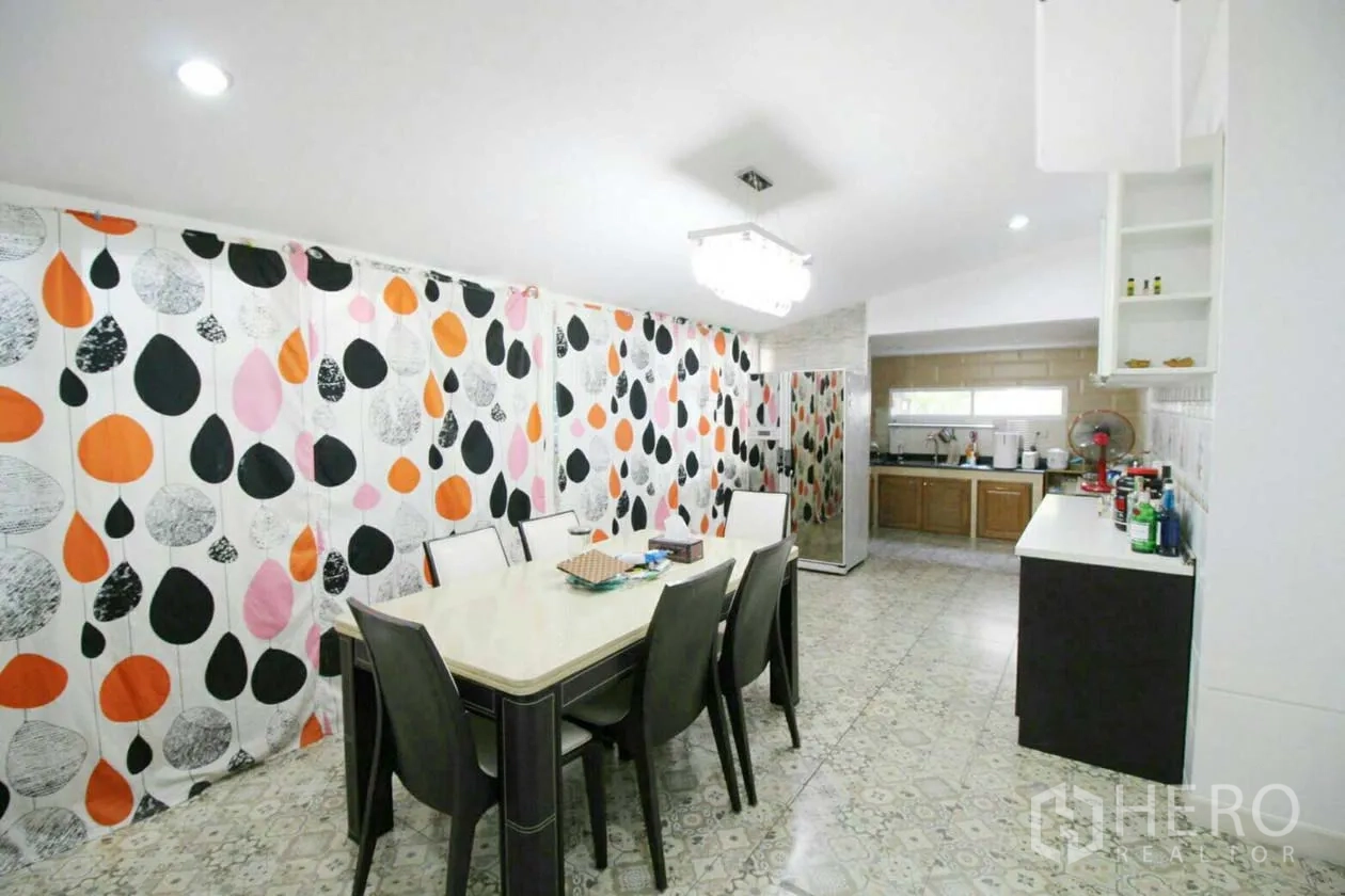 บ้าน ให้เช่าหรือขายในLat Krabang, Bangkok - ห้องอาหารสว่าง โต๊ะยาว ผ้าม่านลายใบไม้สีสันสด ใกล้โซนครัว
