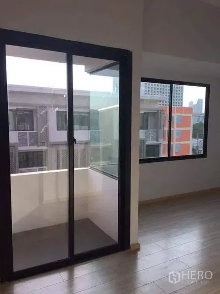 Townhouse for sale in Yan Nawa, Bangkok - Close-up of balcony access via sliding glass door beside a windowed corner of the room.