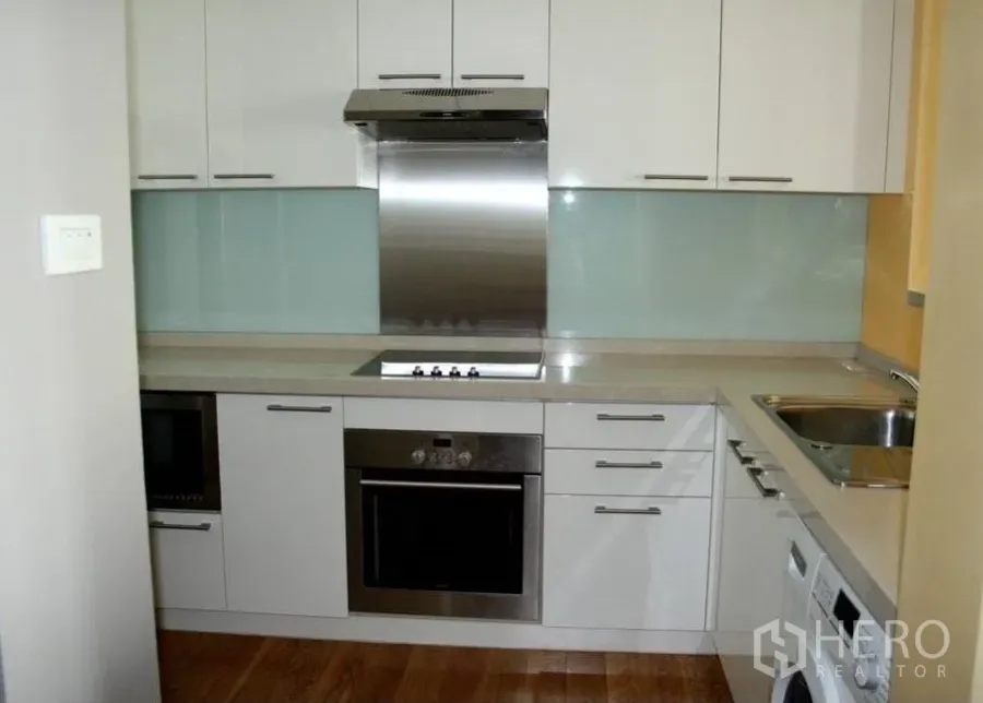 公寓 出租或出售在Watthana, Bangkok - 白色L形厨房，带内置烤箱、电炉、玻璃防溅板与木地板。