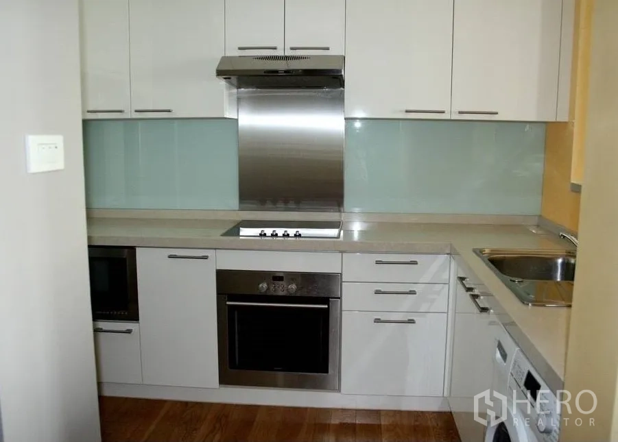 公寓 出租或出售在Watthana, Bangkok - 白色L形厨房，带内置烤箱、电炉、玻璃防溅板与木地板。