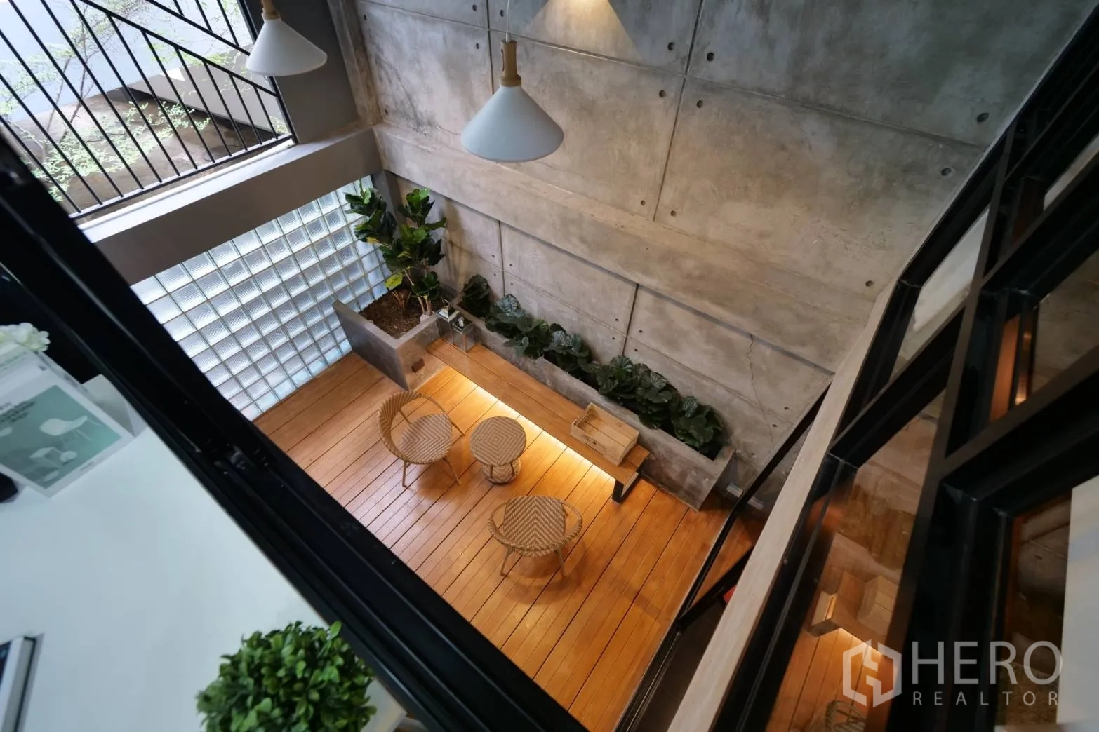 Townhouse for rent in Khlong Toei, Bangkok - Double-height atrium courtyard viewed from above with planters and rattan chairs on a wood deck.