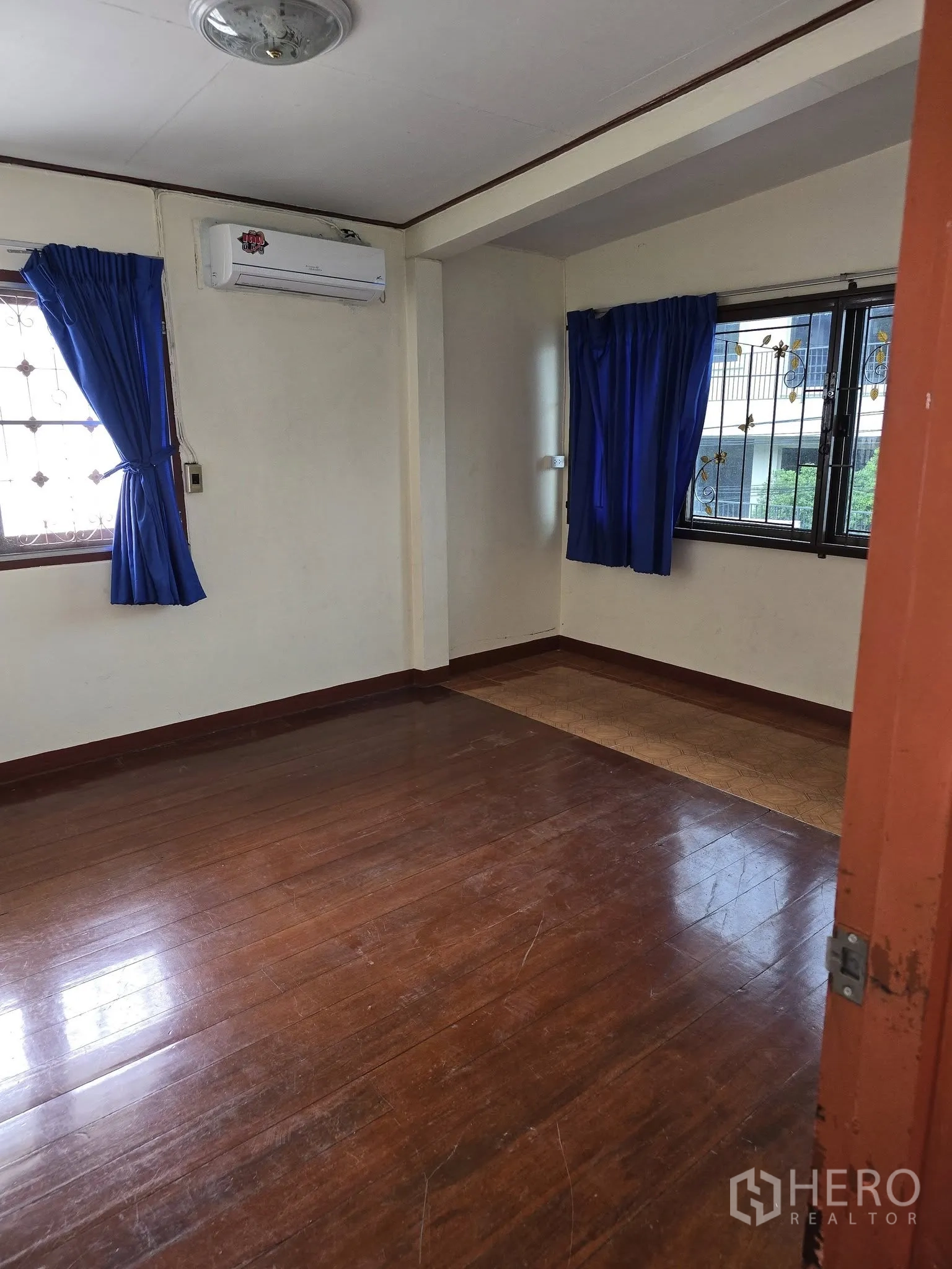 Home Office for rent in Wang Thonglang, Bangkok - Corner bedroom with air conditioner, wood floors and two windows with blue drapes.