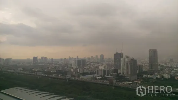Condominium for rent in Ratchathewi, Bangkok - High‑floor view of central Bangkok skyline with greenery and roads under a cloudy sky.