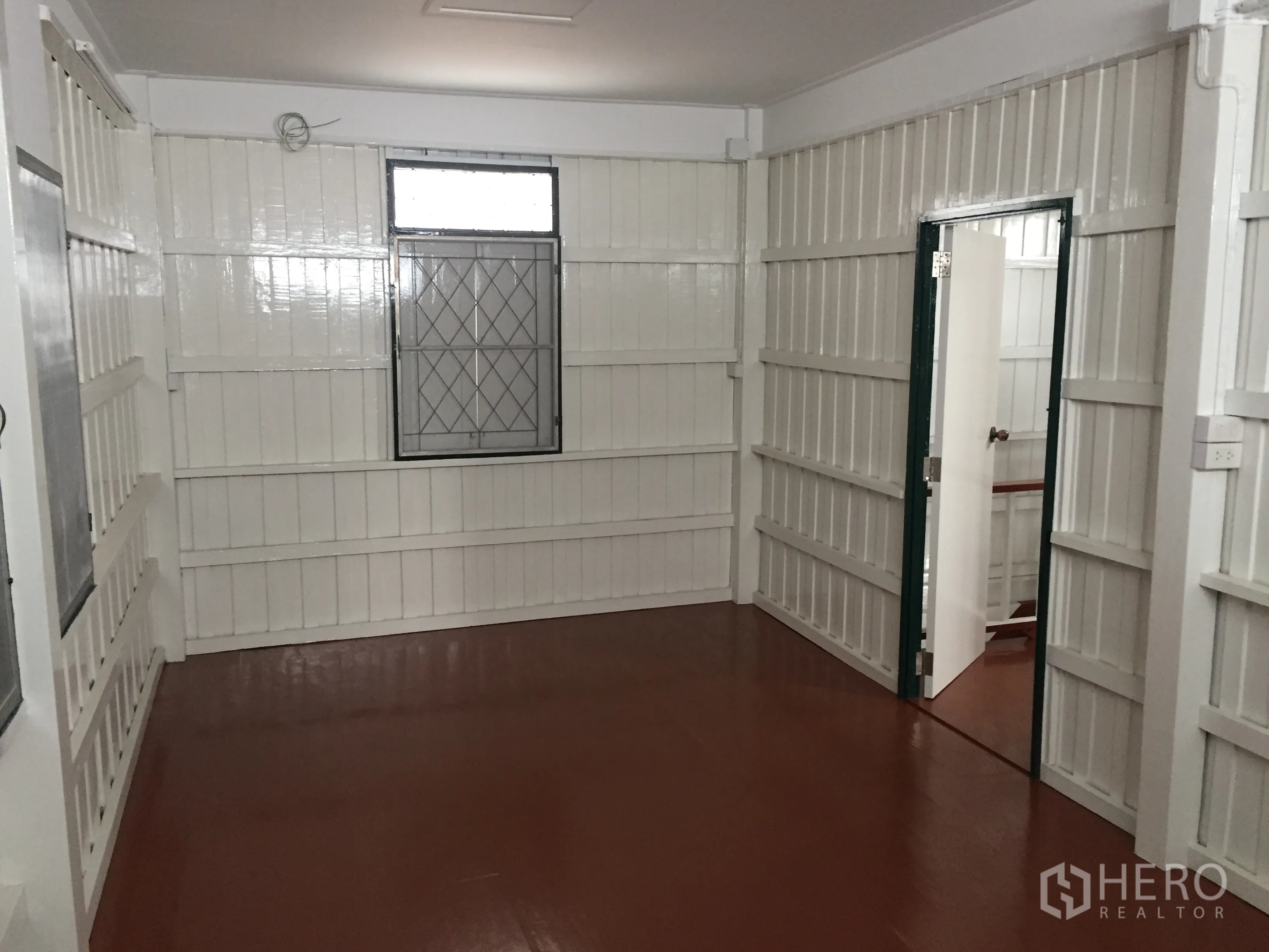 Detached House for rent in Bang Rak, Bangkok - Upstairs room featuring glossy white paneled walls, lattice windows, and a red-brown painted floor.