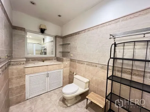 Detached House for rent in Chatuchak, Bangkok - Neutral-toned tiled bathroom with vanity, mirror and toilet.