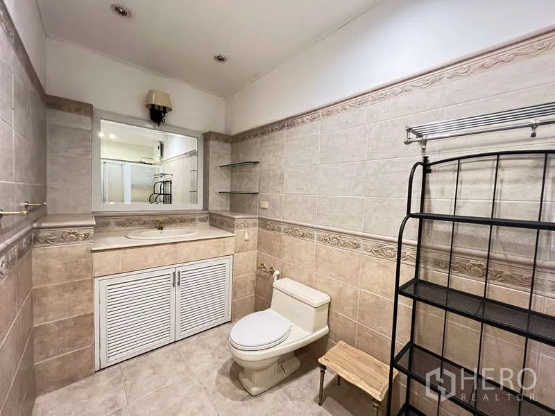 Detached House for rent in Chatuchak, Bangkok - Neutral-toned tiled bathroom with vanity, mirror and toilet.