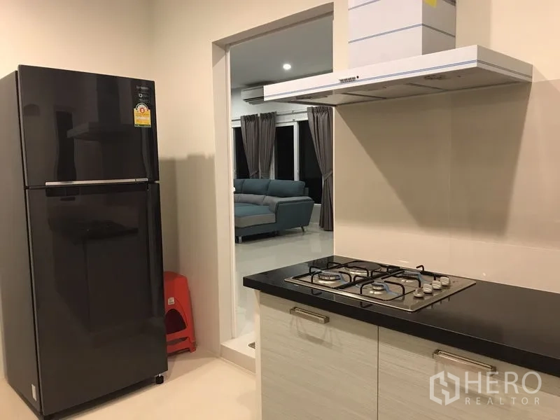 Detached House for rent or sale in Bang Na, Bangkok - Kitchen with gas stove and refrigerator opening toward the living area.