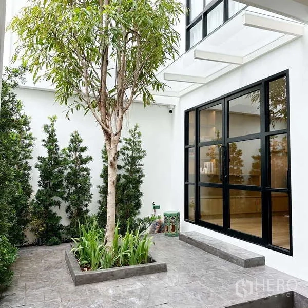 Townhouse for sale in Watthana, Bangkok - Private courtyard with tree planter, greenery and black-framed sliding glass doors.