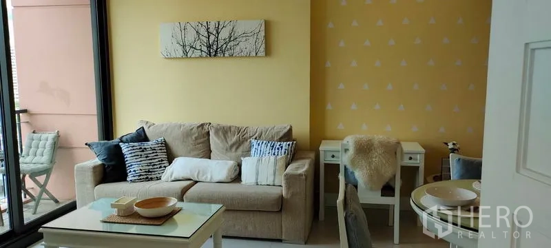 คอนโด ให้เช่าหรือขายในKhlong Toei, Bangkok - ห้องนั่งเล่นอบอุ่น โซฟาสีเบจ โต๊ะกลาง เปิดออกสู่ระเบียงที่ Aguston Sukhumvit 22