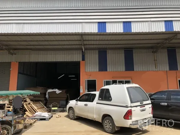 货栈 出租在Khlong Luang, Pathum Thani - 空銮区金属外墙仓库外观，屋顶挑高，宽幅卷闸门，带雨棚装卸区与混凝土停车区。