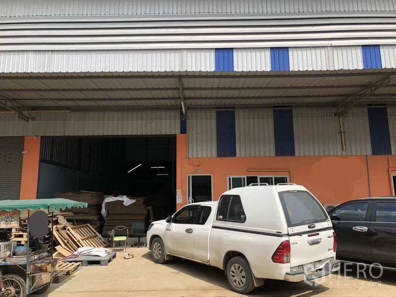 货栈 出租在Khlong Luang, Pathum Thani - 空銮区金属外墙仓库外观，屋顶挑高，宽幅卷闸门，带雨棚装卸区与混凝土停车区。