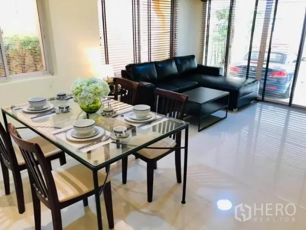 Detached House for rent in Watthana, Bangkok - Bright dining and living area with a glass dining table and black leather sectional beside large windows.