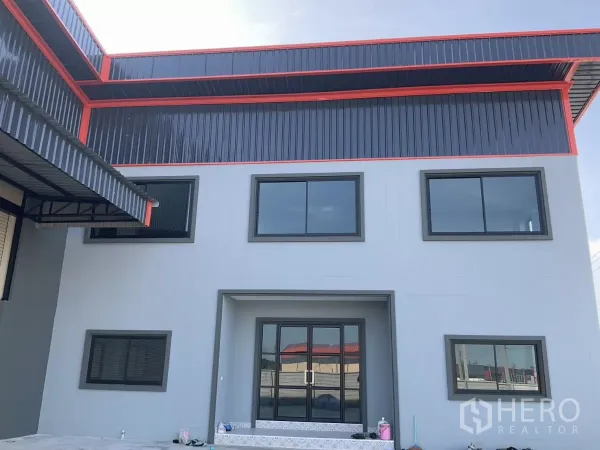 工厂 出售在Samut Sakhon - 办公楼正立面近景，玻璃入口与大窗，带钢结构雨棚