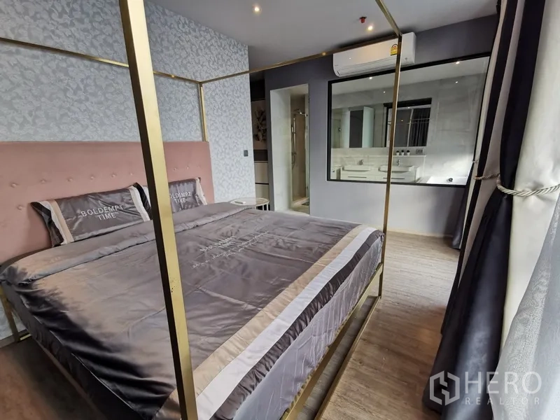 Condominium for rent or sale in Watthana, Bangkok - Primary bedroom with a four-poster bed, soft pink headboard, large window, and access to the en-suite bathroom.