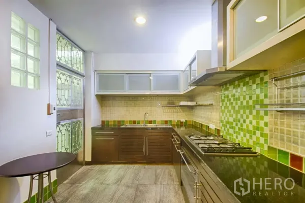 Townhouse for rent in Watthana, Bangkok - L-shaped kitchen with gas hob, range hood and green tiled backsplash.