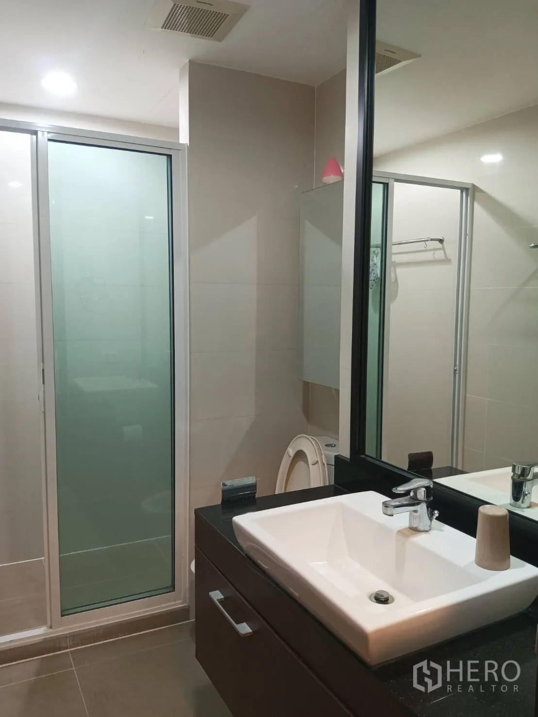 Condominium for sale in Chatuchak, Bangkok - Modern bathroom with glass-enclosed shower, large mirror and vanity sink.