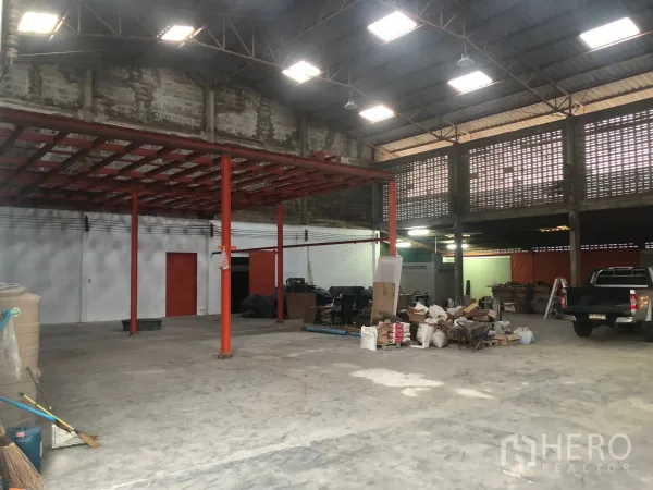 Warehouse for rent in Min Buri, Bangkok - Large storage hall with red steel columns, partial mezzanine frame and wide loading space on concrete floor.
