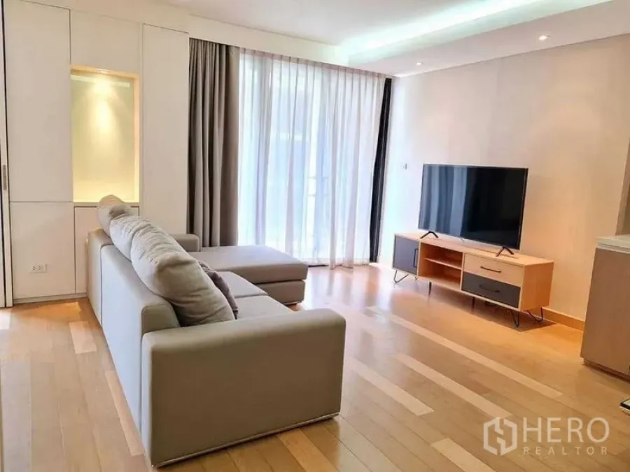 คอนโด ให้เช่าในWatthana, Bangkok - พื้นที่นั่งเล่นพร้อมโซฟาตัวแอล ชั้นวางทีวี และม่านสูงจรดเพดานรับแสงธรรมชาติ