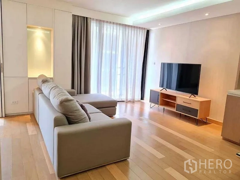 คอนโด ให้เช่าในWatthana, Bangkok - พื้นที่นั่งเล่นพร้อมโซฟาตัวแอล ชั้นวางทีวี และม่านสูงจรดเพดานรับแสงธรรมชาติ