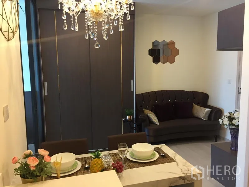 Condominium for rent in Huai Khwang, Bangkok - Dining area with crystal chandelier facing a cozy sofa and sliding partition doors.