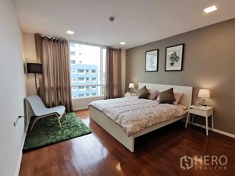 Condominium for sale in Khlong Toei, Bangkok - Spacious bedroom with king bed, large window, and wood floors overlooking city.