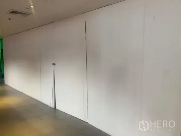 Retail Space for rent - White hoarding frontage of a vacant retail unit along an indoor mall corridor with ceiling lights.