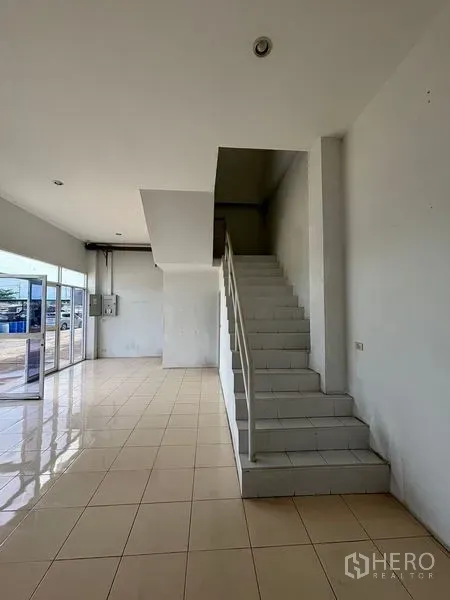 Warehouse for rent in Phra Samut Chedi, Samut Prakan - Ground-floor office area with floor-to-ceiling glass entry and staircase to an upper office.