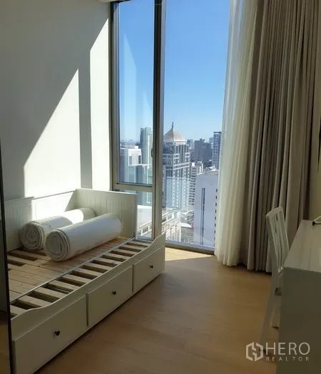 Condominium for rent in Pathum Wan, Bangkok - Second bedroom with single bed frame, desk and full-height window overlooking the city.