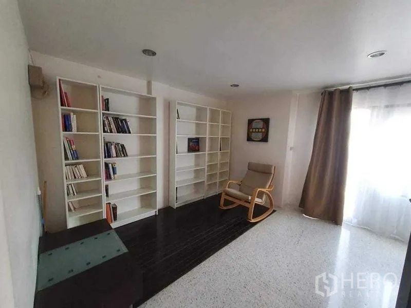 Townhouse for rent or sale in Bang Kho Laem, Bangkok - Reading nook with white bookcases, lounge chair and soft daylight through curtains.