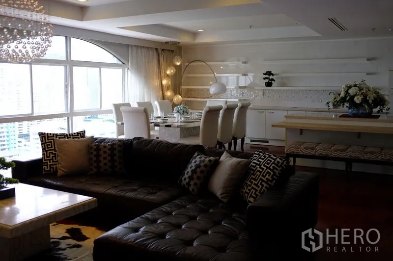 公寓 出租在Watthana, Bangkok - 开放式客餐厅，皮质转角沙发、水晶吊灯与大幅采光窗。