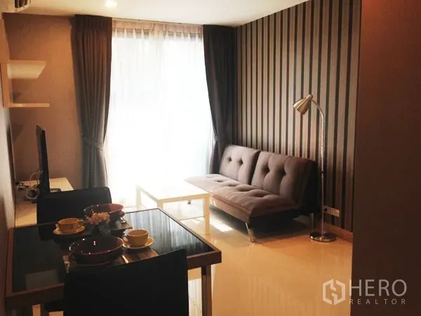 Condominium for rent or sale in Mueang Samut Prakan, Samut Prakan - Open-plan living area with striped accent wall, sofa, dining set and large window.