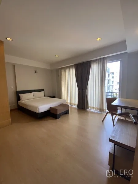 อพาร์ทเมนท์ ให้เช่าในWatthana, Bangkok - ห้องนอนเตียงคู่พร้อมโต๊ะทำงานและประตูกระจกบานเลื่อนออกสู่ระเบียง.