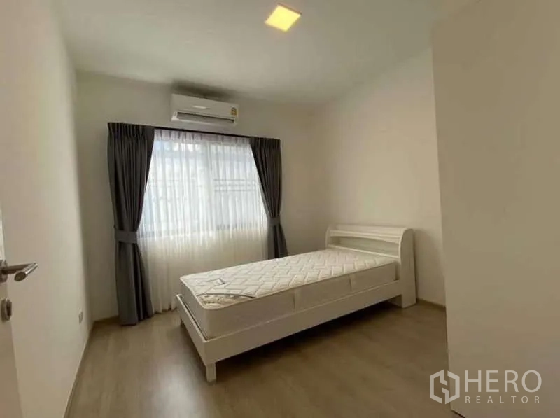 Townhouse for rent in Bang Phli, Samut Prakan - Cozy secondary bedroom with single bed, air conditioner and sheer curtains.