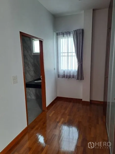 Detached House for rent in Prawet, Bangkok - Bedroom corner with an ensuite door, window and curtains on hardwood flooring.
