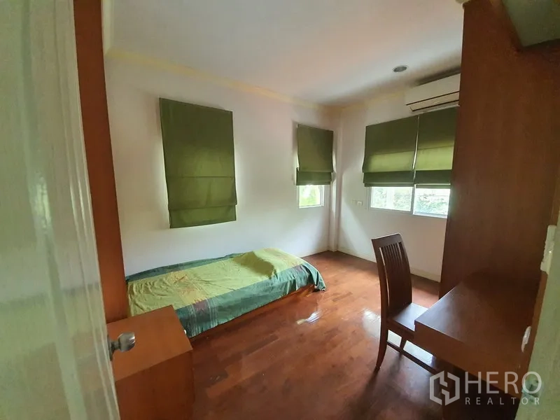 บ้าน ให้เช่าในLat Krabang, Bangkok - ห้องนอนเล็กอบอุ่น พื้นไม้ โต๊ะทำงาน และมู่ลี่สีเขียวที่หน้าต่างมุมห้อง.