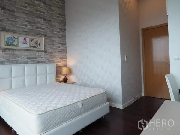 Condominium for rent in Ratchathewi, Bangkok - Bright bedroom with white upholstered bed, bedside lamp and textured gray feature wall.