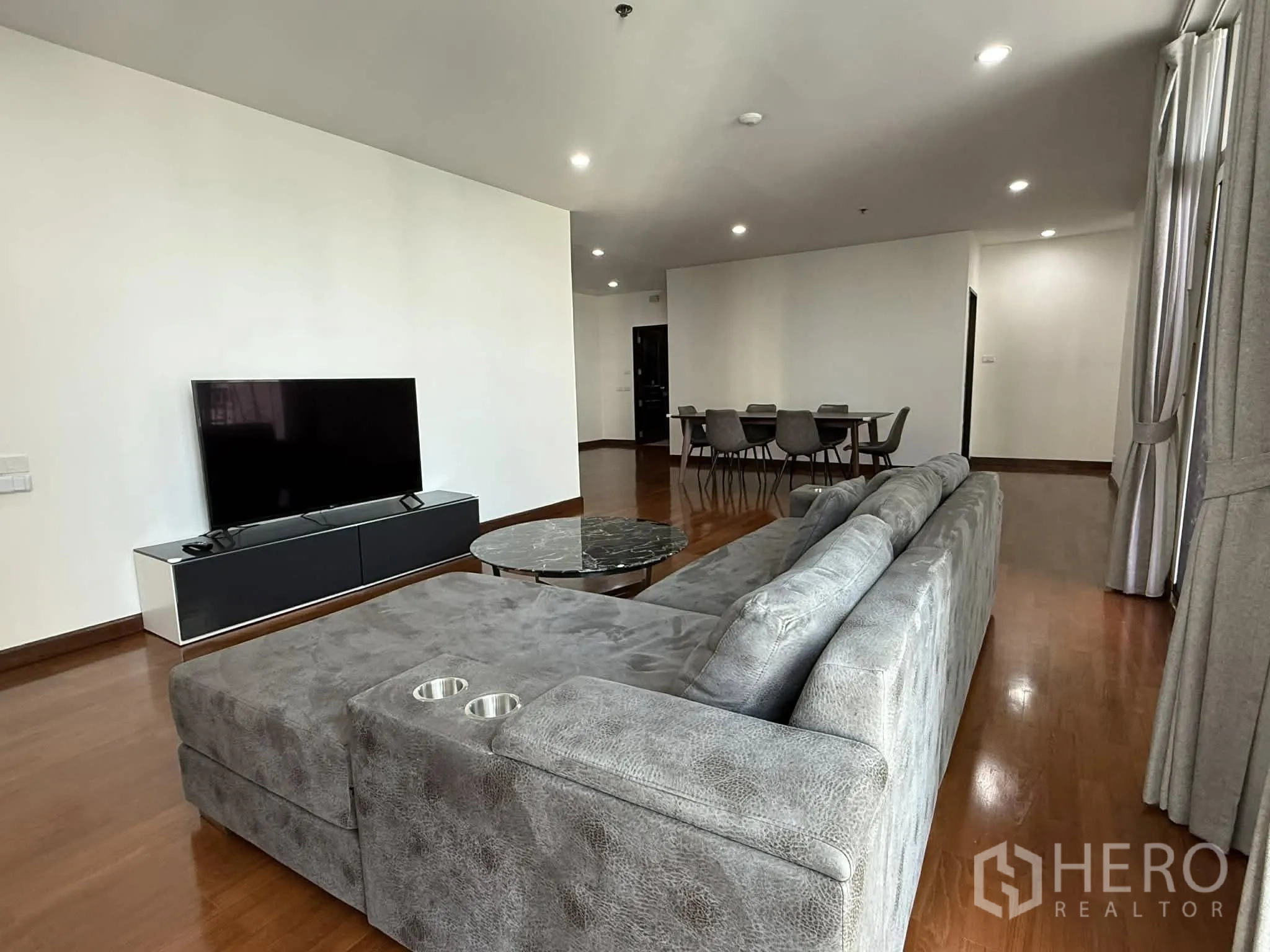 公寓 for rent in Pathum Wan, Bangkok - 客厅设大型灰色转角沙发、电视柜与圆形大理石茶几。