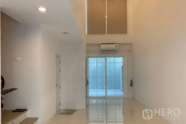 ทาวน์เฮาส์ ให้เช่าในBang Na, Bangkok - ห้องนั่งเล่นเพดานสูง พื้นกระเบื้องเงา แอร์ และหน้าต่างสูงเหนือประตูกระจกบานเลื่อน