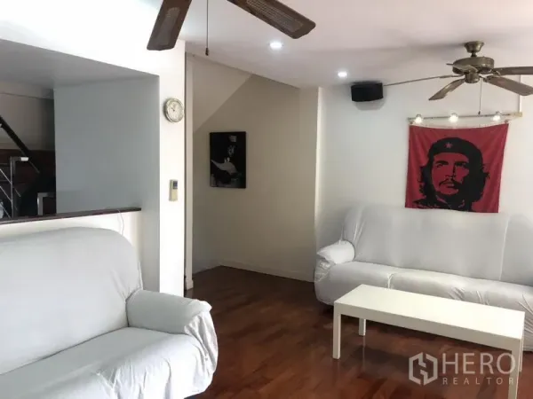 ทาวน์เฮาส์ ให้เช่าหรือขายในBangkok - ห้องนั่งเล่นอบอุ่น โซฟาสีขาว พื้นไม้ และพัดลมเพดาน มีงานศิลป์ติดผนัง