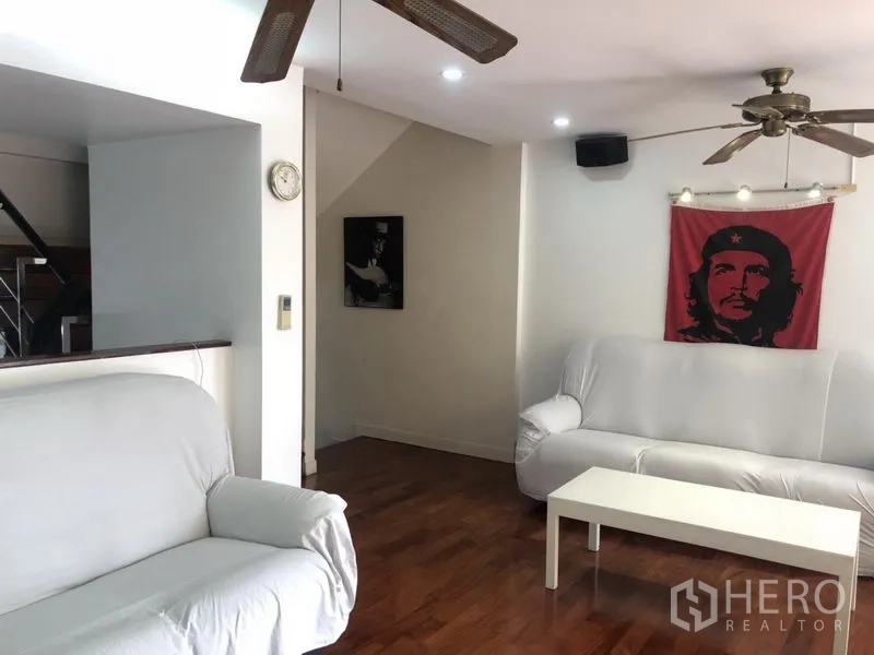 ทาวน์เฮาส์ ให้เช่าหรือขายในBangkok - ห้องนั่งเล่นอบอุ่น โซฟาสีขาว พื้นไม้ และพัดลมเพดาน มีงานศิลป์ติดผนัง