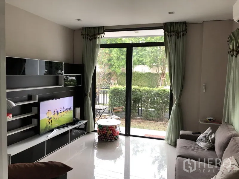 独立式住宅 出租在Saphan Sung, Bangkok - 采光明亮的客厅，配电视墙、沙发与可通往花园的推拉落地门。