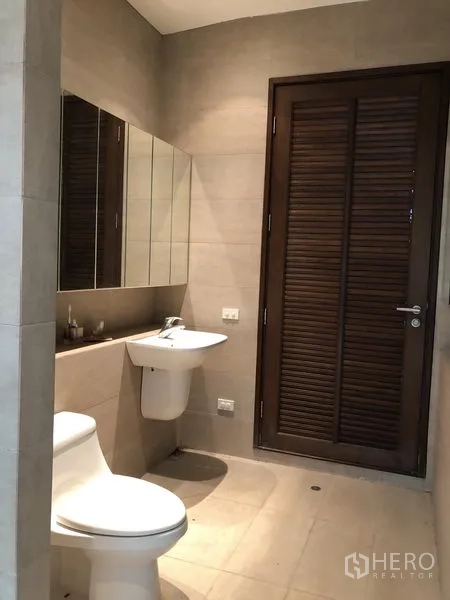 Factory for rent in Pathum Thani - Tiled restroom with toilet, wall-hung basin, mirrored cabinet and wooden louvered door.