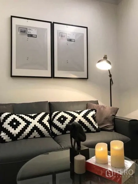 คอนโด ให้เช่าหรือขายในRatchathewi, Bangkok - โซฟาสีเทาพร้อมหมอนลายขาวดำ โคมไฟตั้งพื้น กรอบรูป และเทียนบนโต๊ะกระจก