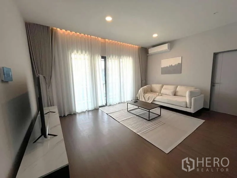 Detached House for rent or sale in Bang Phli, Samut Prakan - Upstairs family room with sofa, TV console and sheer curtains opening to a balcony.