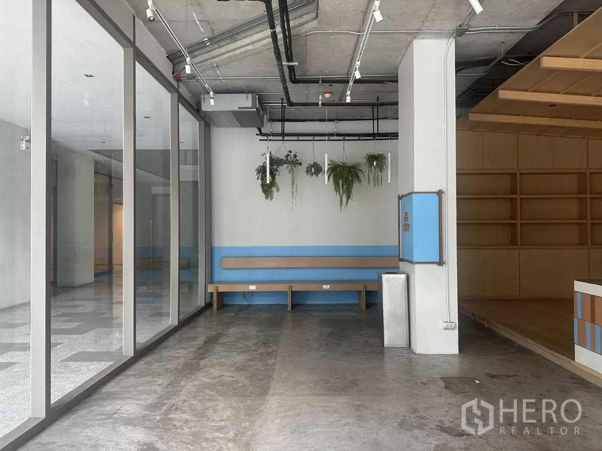 พื้นที่ขายปลีก ให้เช่า - มุมติดกระจกพร้อมม้านั่งยาวและต้นไม้ตกแต่ง ข้างชั้นวางไม้