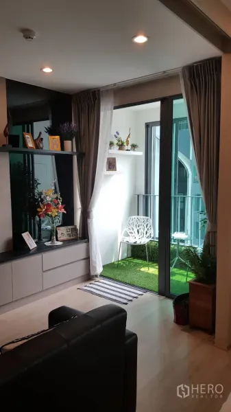 公寓 出租在Bang Rak, Bangkok - 推拉玻璃门通向铺人造草的阳台，配白色椅子。