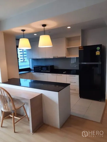 公寓 出租在Watthana, Bangkok - 现代白色厨房，黑色石材台面与早餐吧台，吊灯与城市景观。