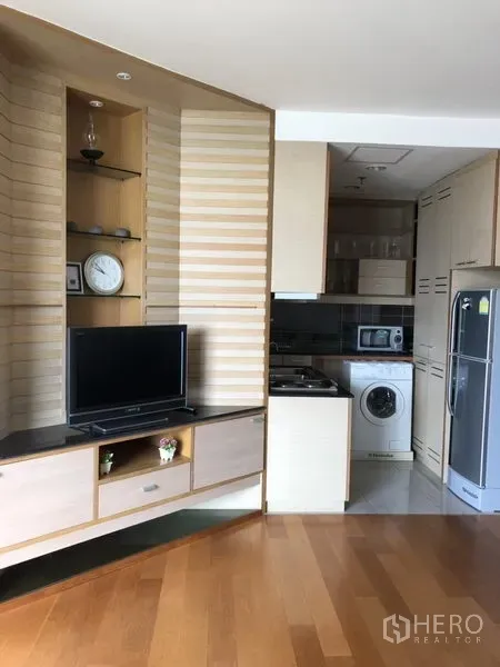 Condominium for rent in Bang Kho Laem, Bangkok - Open-plan living with built-in TV unit and a compact kitchen featuring a washing machine and fridge.