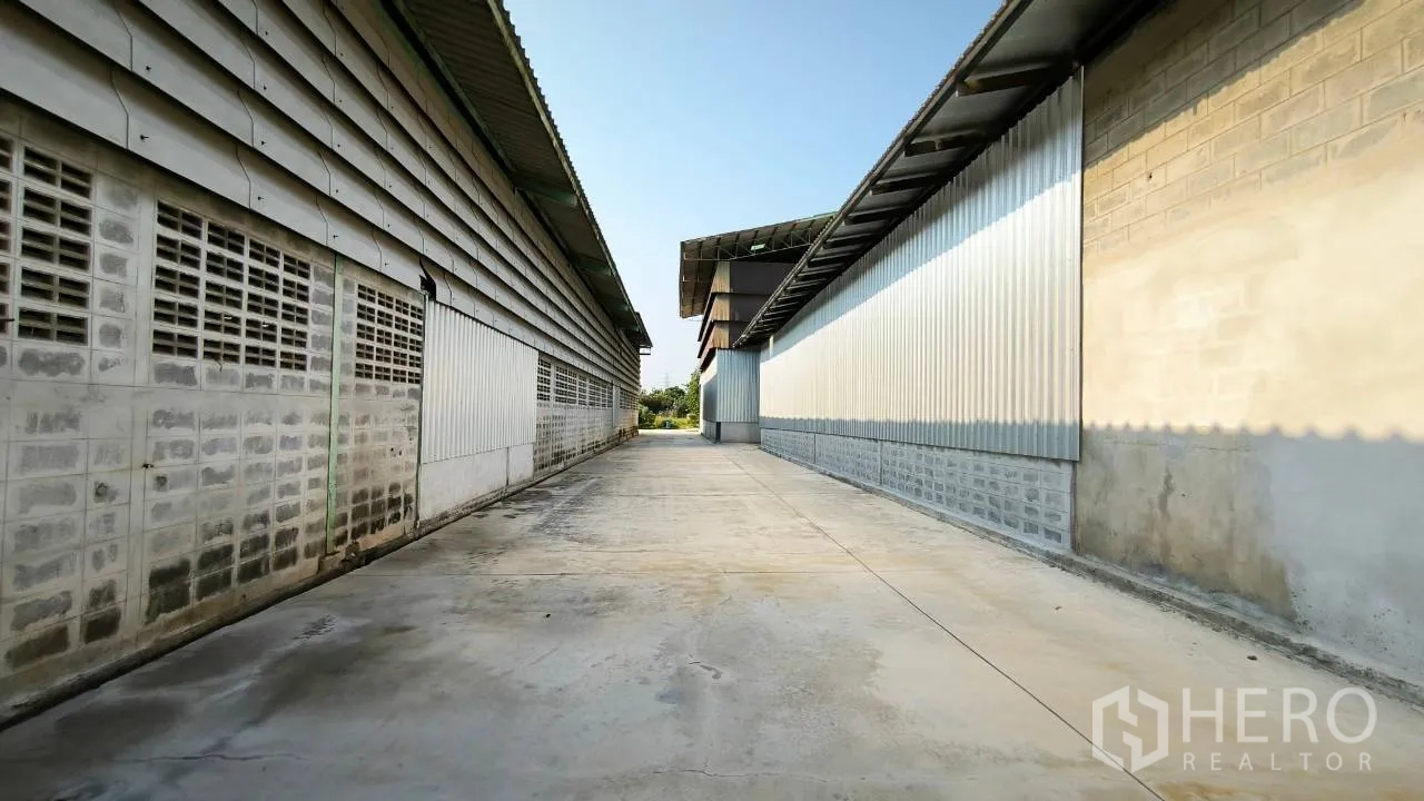 Factory for rent in Mueang Samut Prakan, Samut Prakan - Concrete driveway between corrugated factory buildings for truck circulation.