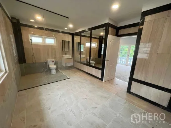 Detached House for sale in Bang Na, Bangkok - Oversized bathroom with glass-enclosed shower, toilet and vanity in beige-and-black tiles.